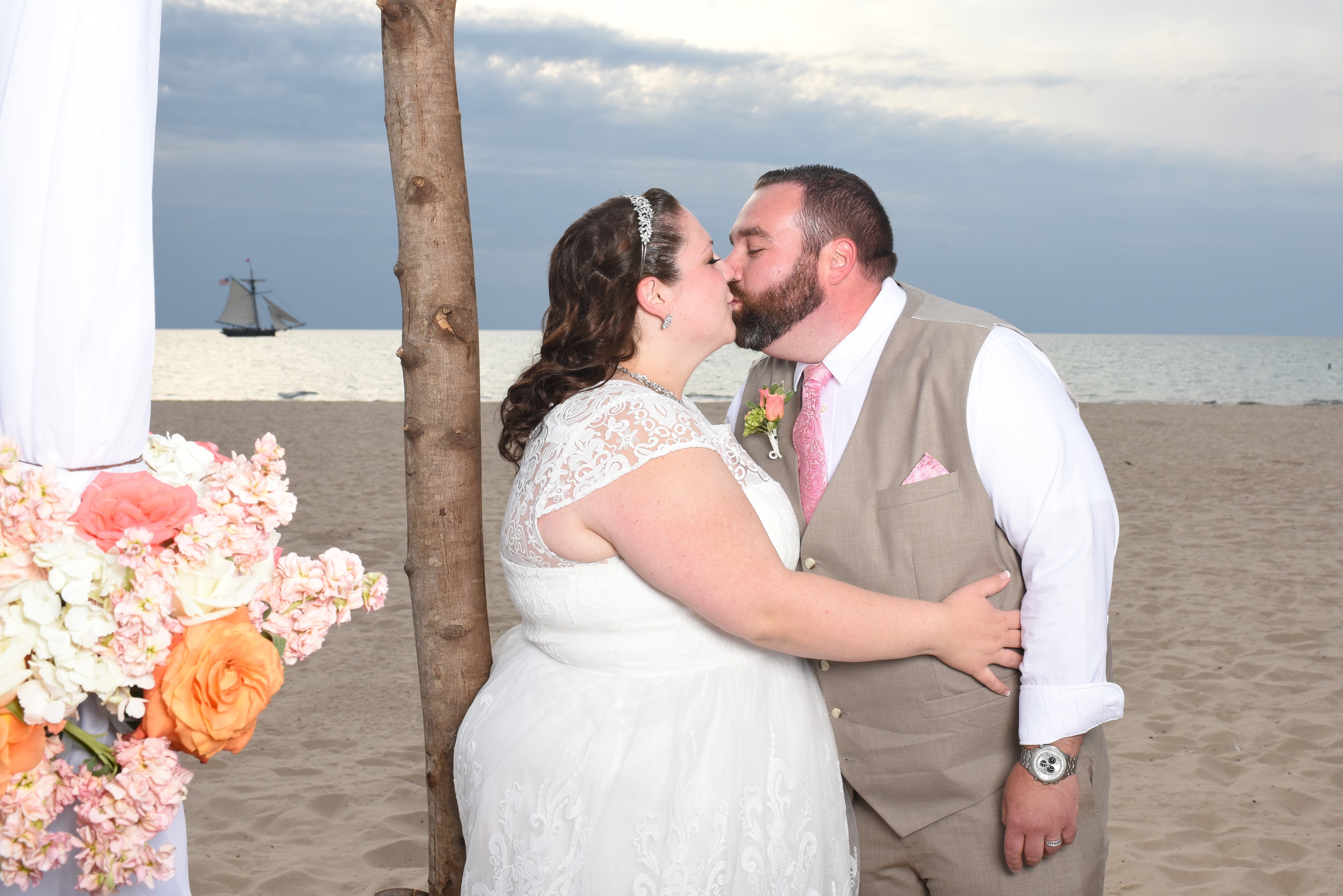 Newleyweds kissing with arbor and sailboat in background