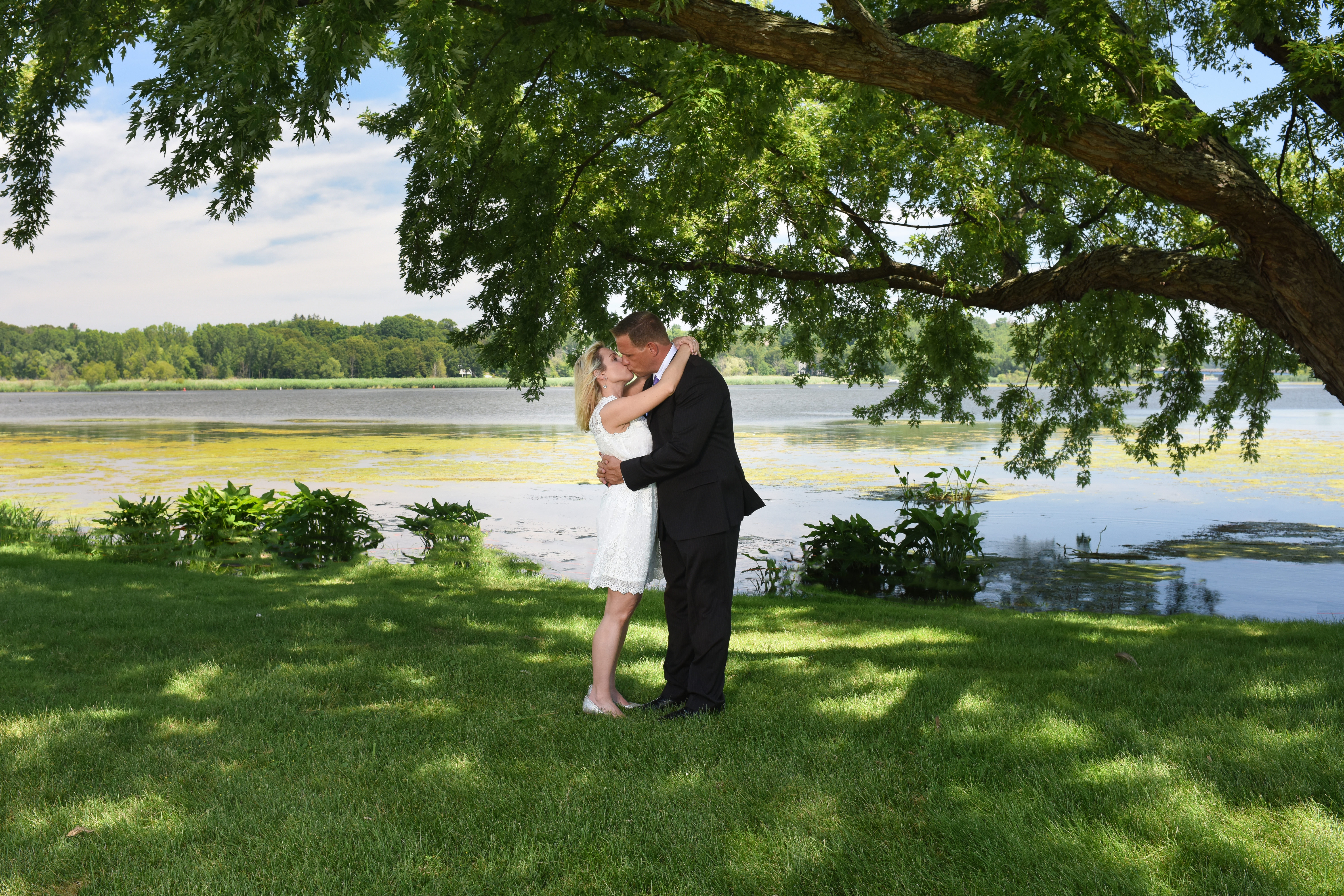bride and groom kissing with water and trees in background